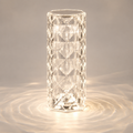 Clear faceted table lamp glowing on a gray surface with circular light patterns around the base.