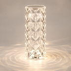 Clear faceted table lamp glowing on a gray surface with circular light patterns around the base.