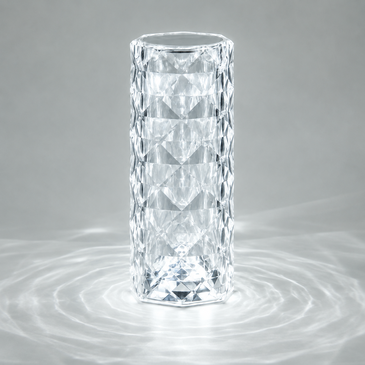 Clear faceted table lamp glowing cool white and casting circular light patterns on a gray surface.