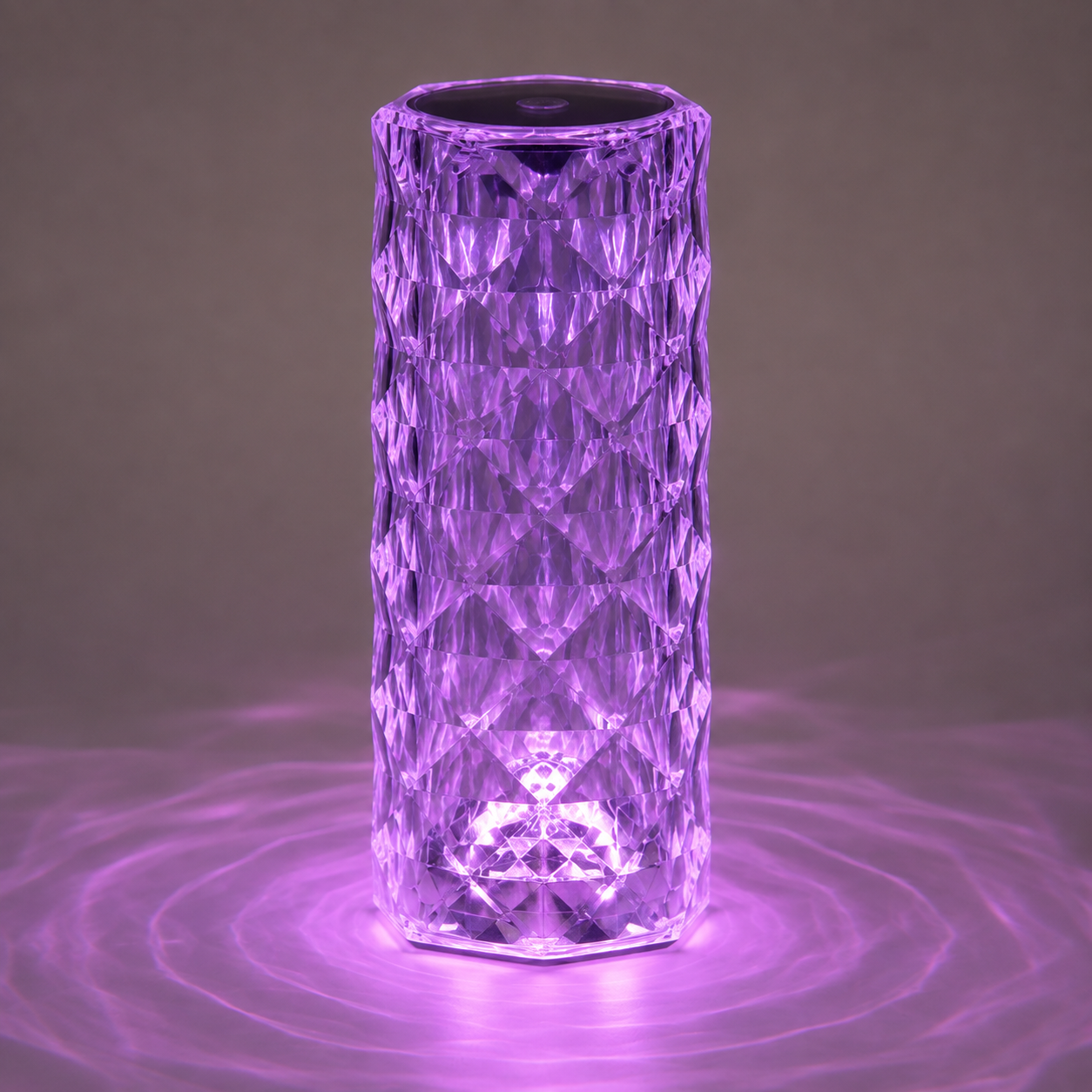 Clear faceted table lamp glowing purple and casting circular light patterns on a gray surface.