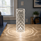 Clear faceted table lamp glowing on a table in a bright living room with a window and sofa.