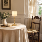 Gold cordless table lamp glowing on a round dining table in a sunlit room.