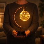 Crescent moon table lamp held with both hands against a softly blurred room.