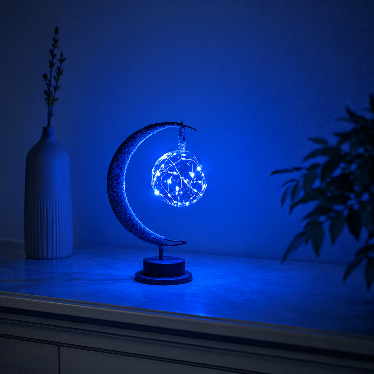 Crescent moon table lamp casting blue light across a console and blue wall.