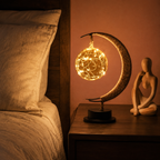 Crescent moon table lamp glowing beside bedding and a small sculpture.