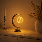 Crescent moon table lamp glowing warmly beside a candlestick and dried flowers.