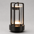 Black cordless lantern table lamp with a clear cylindrical shade, illuminated against a neutral background.