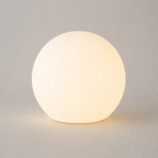 Glowing round table lamp on a plain light gray background with a soft shadow beneath the globe.
