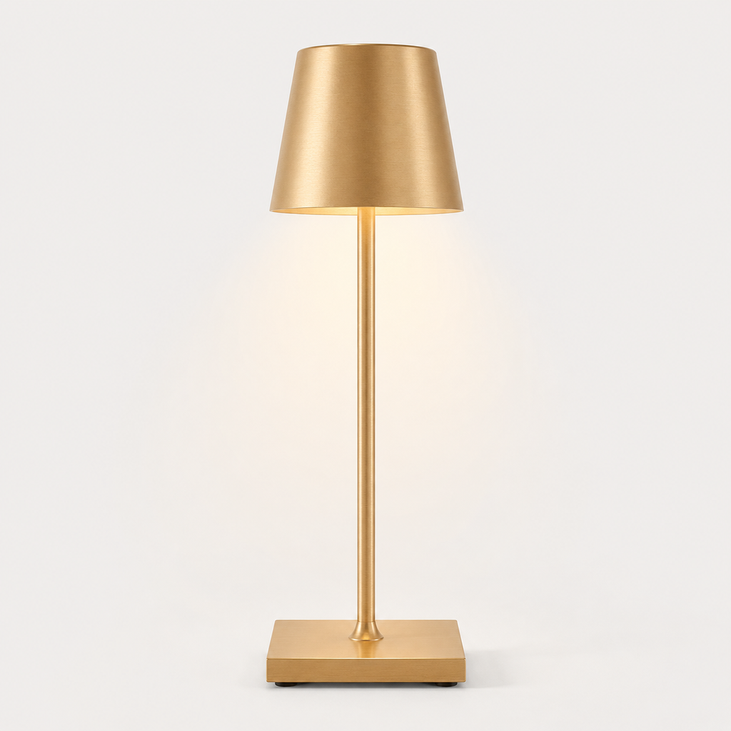 Gold table lamp with a tapered shade, slim stem, square base and warm light on a plain background.
