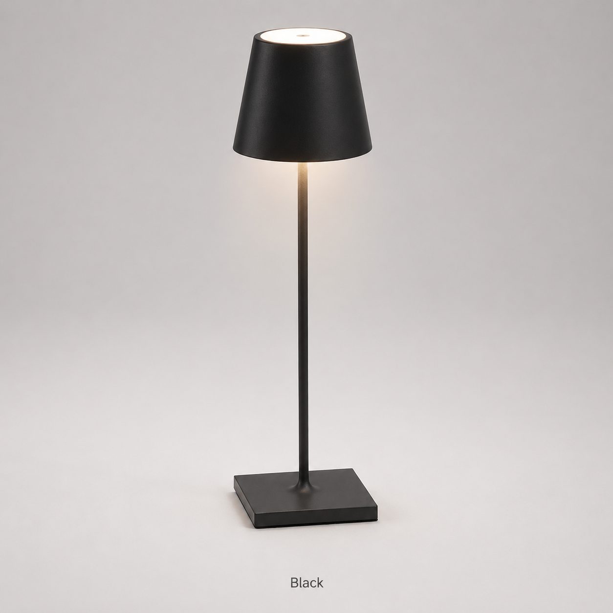 Black table lamp with a tapered shade, slim stem, square base and warm light on a plain background.