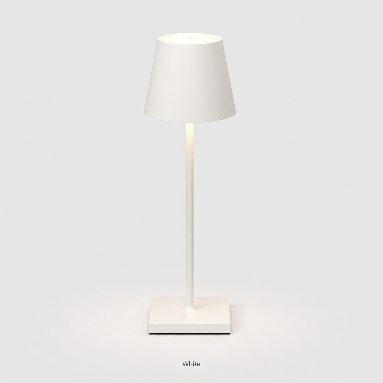 White table lamp with a tapered shade, slim stem, square base and warm light on a plain background.