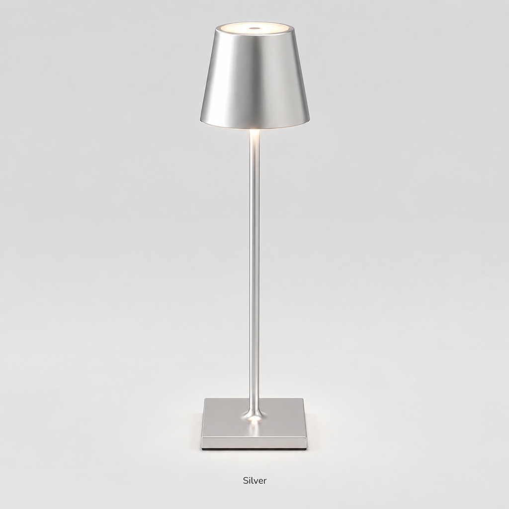 Silver table lamp with a tapered shade, slim stem, square base and warm light on a plain background.