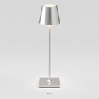 Silver table lamp with a tapered shade, slim stem, square base and warm light on a plain background.