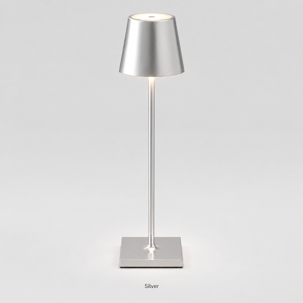 Silver table lamp with a tapered shade, slim stem, square base and warm light on a plain background.