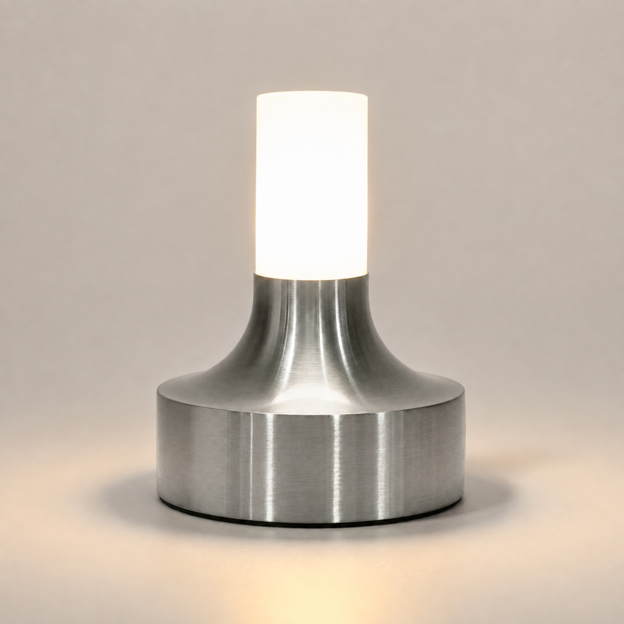 Silver table lamp glowing on a light neutral studio background with a soft shadow.