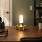 Gold table lamp glowing on a wooden table in a softly lit dining area.