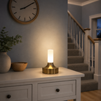 Gold table lamp glowing on a white nightstand beneath a wall clock.