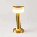 Gold table lamp with a glowing white cylindrical shade on a plain light gray background.