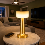 Gold table lamp lit on a round coffee table in a warmly furnished living room.