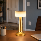 Gold table lamp glowing on a wooden desk beside a pencil cup and laptop.