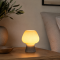 Smoke gray ribbed glass mushroom table lamp glowing on a wood table.