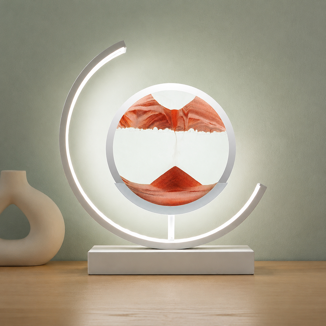Red quicksand table lamp with a white frame glowing on a blond oak tabletop.
