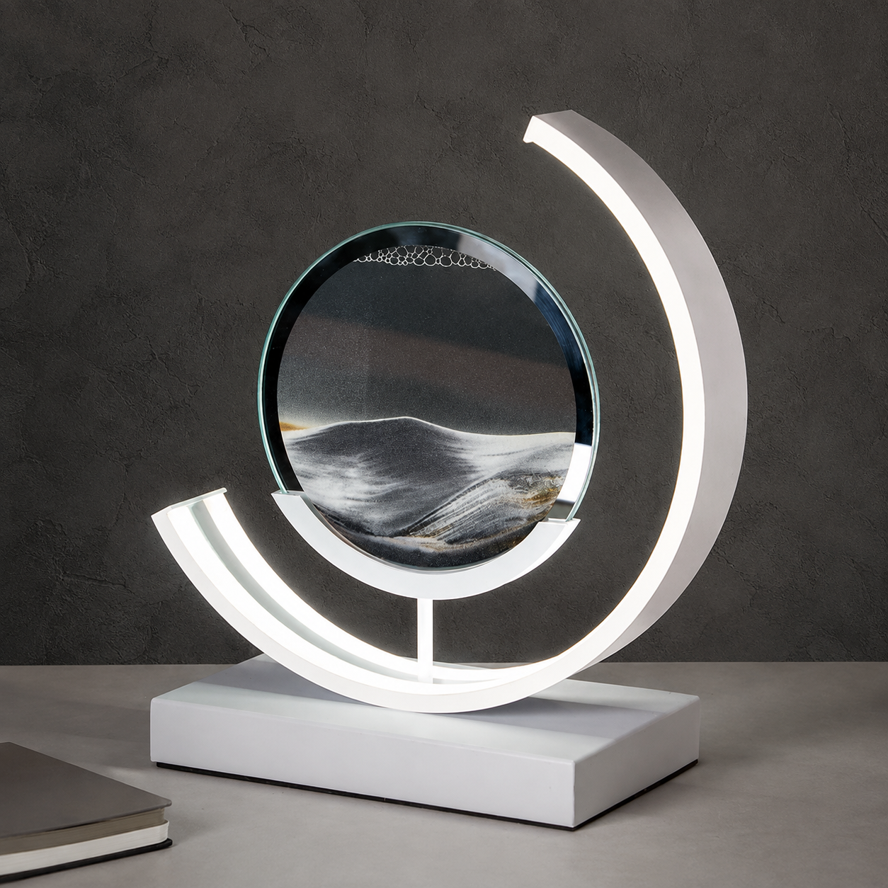 Black quicksand table lamp with a white curved frame on a gray tabletop.