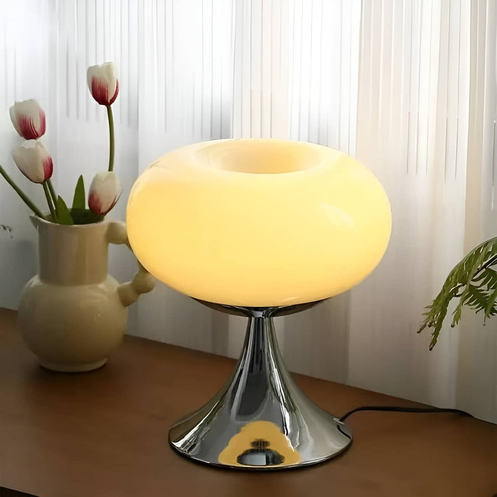Beige donut table lamp glowing beside tulips at a window.