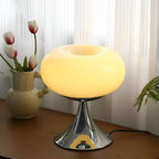 Beige donut table lamp glowing beside tulips at a window.