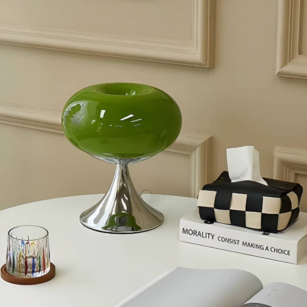 Green donut table lamp beside a glass and patterned tissue holder.