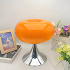 Orange donut table lamp beside flowers and framed artwork.