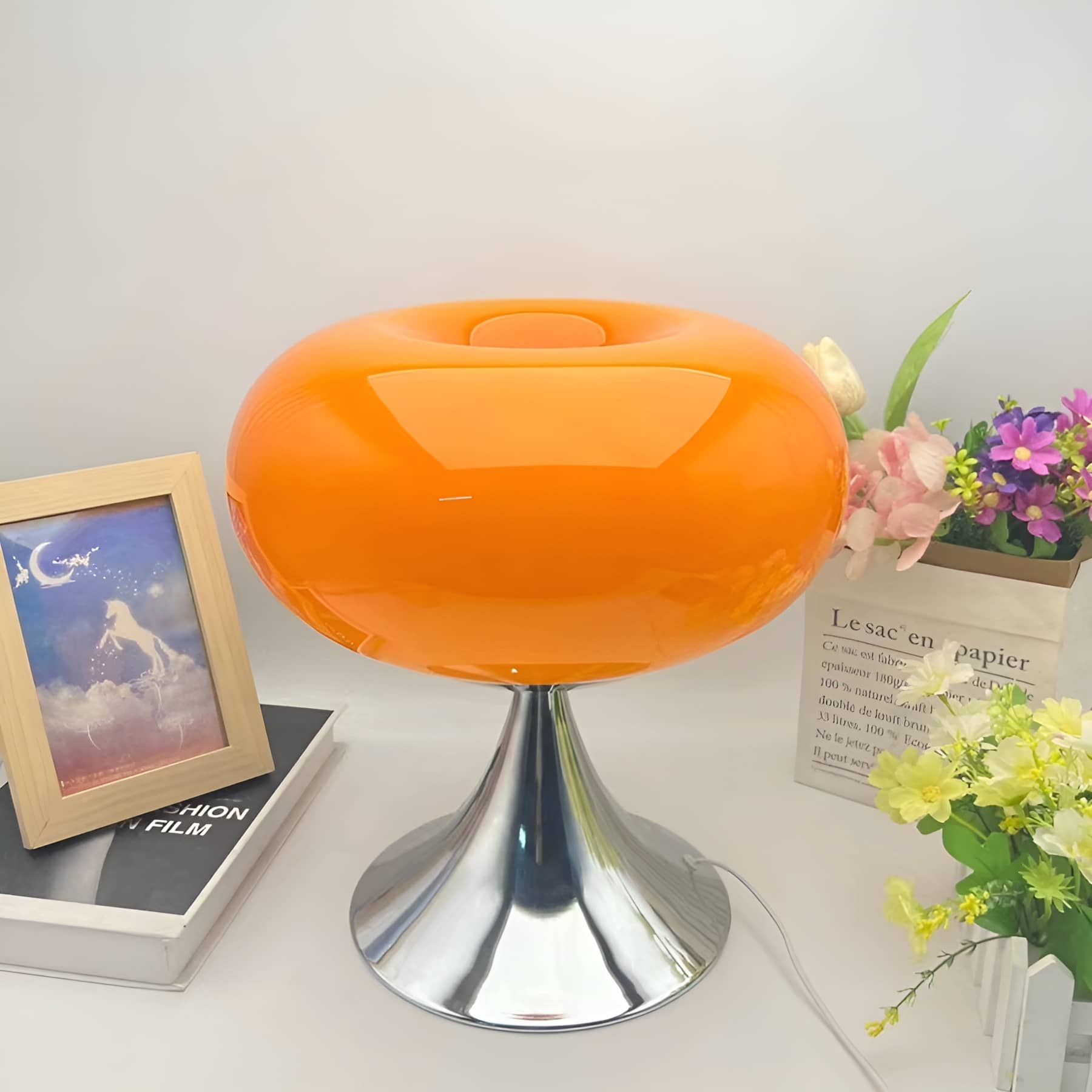 Orange donut table lamp beside flowers and framed artwork.