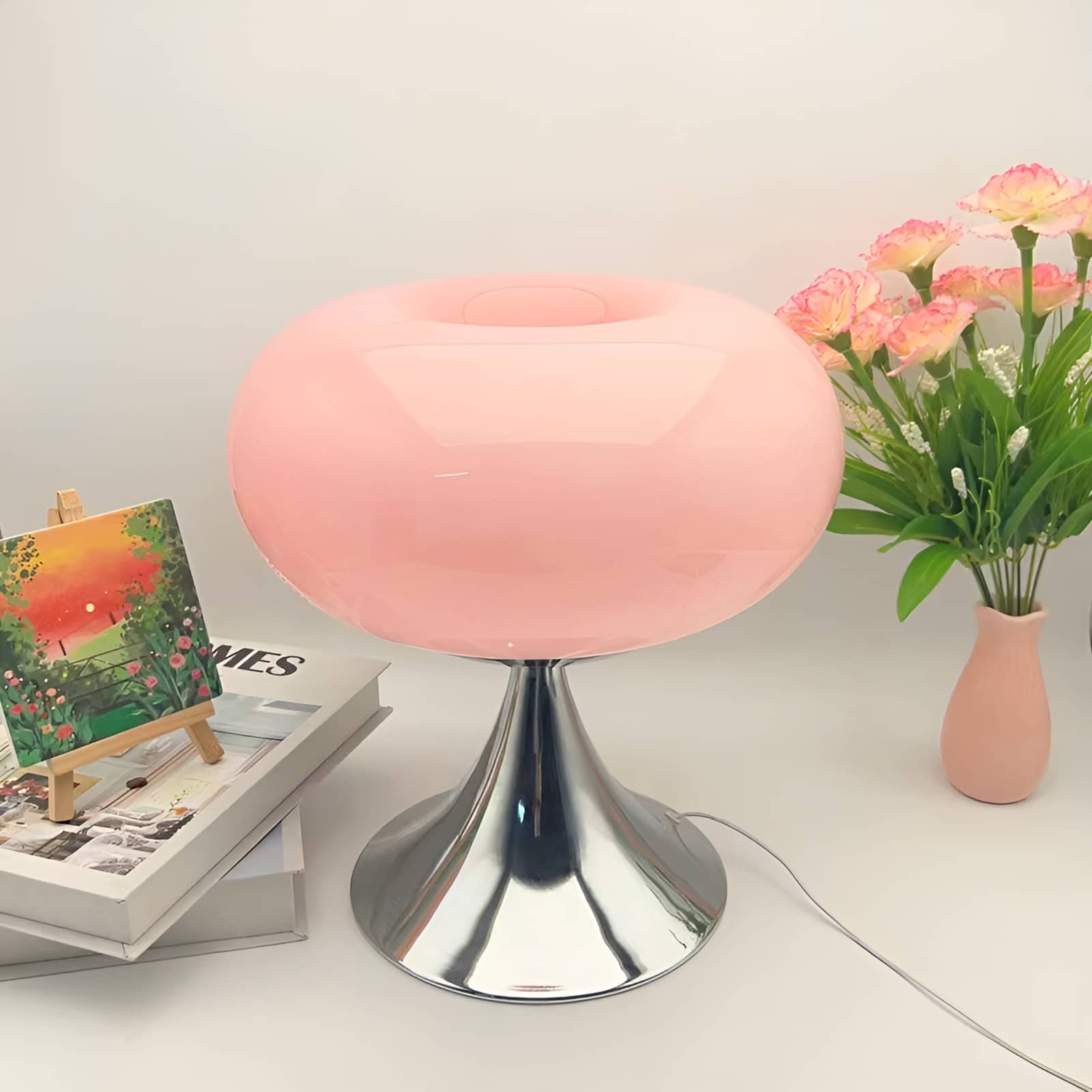 Pink donut table lamp with a polished pedestal beside flowers.