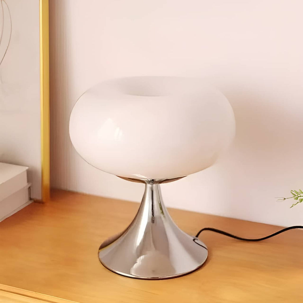 White donut table lamp glowing on a wood bedside surface.