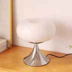 White donut table lamp glowing on a wood bedside surface.