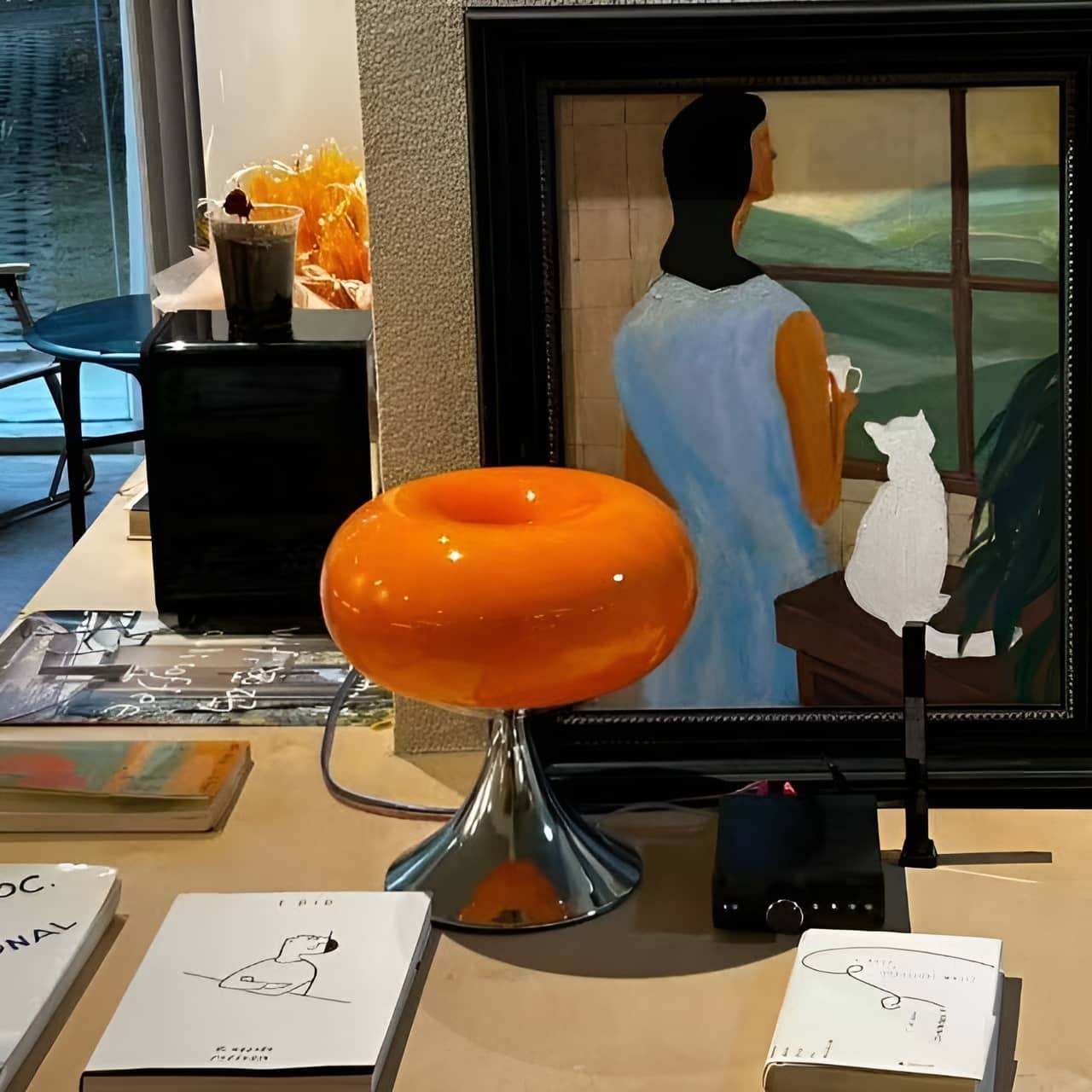 Orange donut table lamp on a cabinet beneath framed artwork.