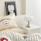 White donut table lamp beside a bed with patterned cushions.
