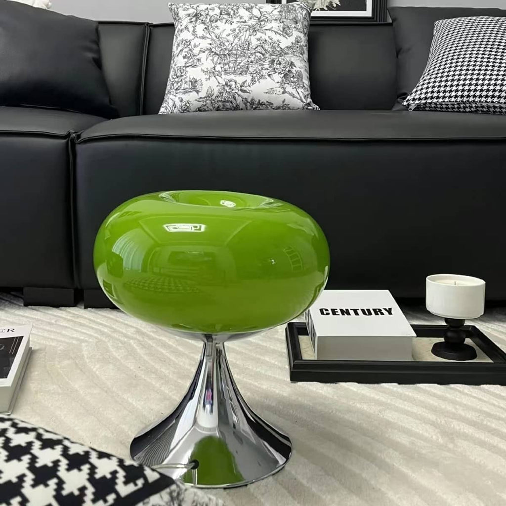 Green donut table lamp on a coffee table in front of a dark sofa.