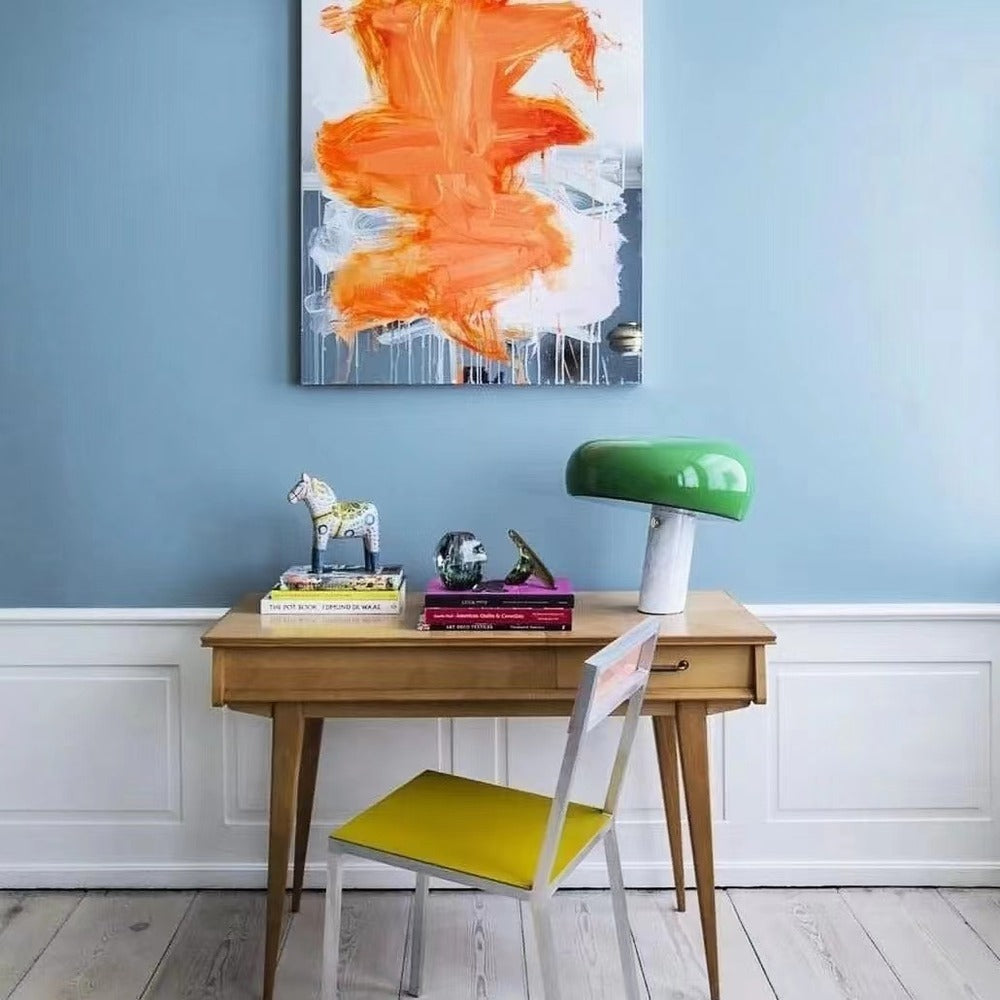 Green marble table lamp on a wooden writing desk against a blue wall.