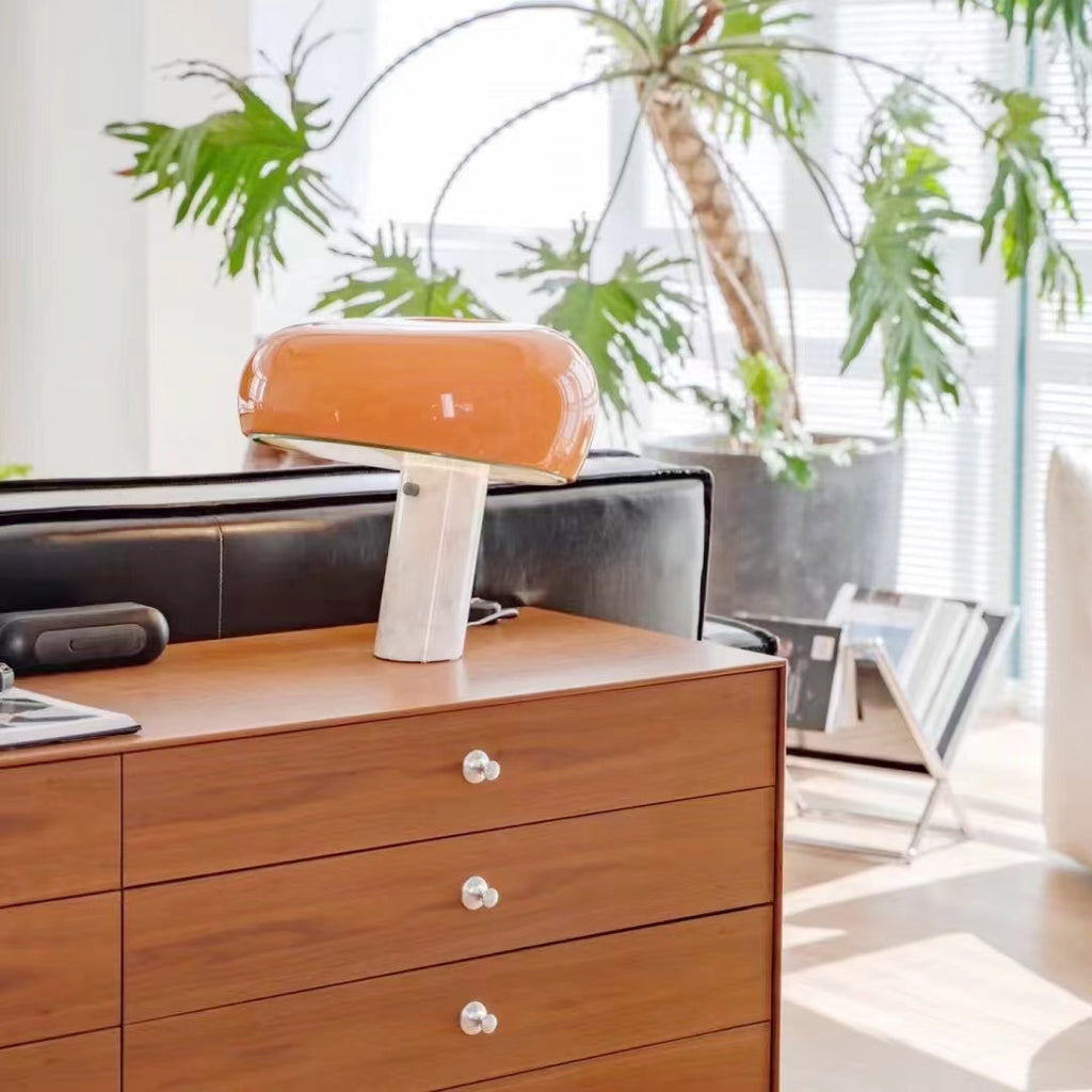 Orange marble table lamp on a wood cabinet beside indoor plants.