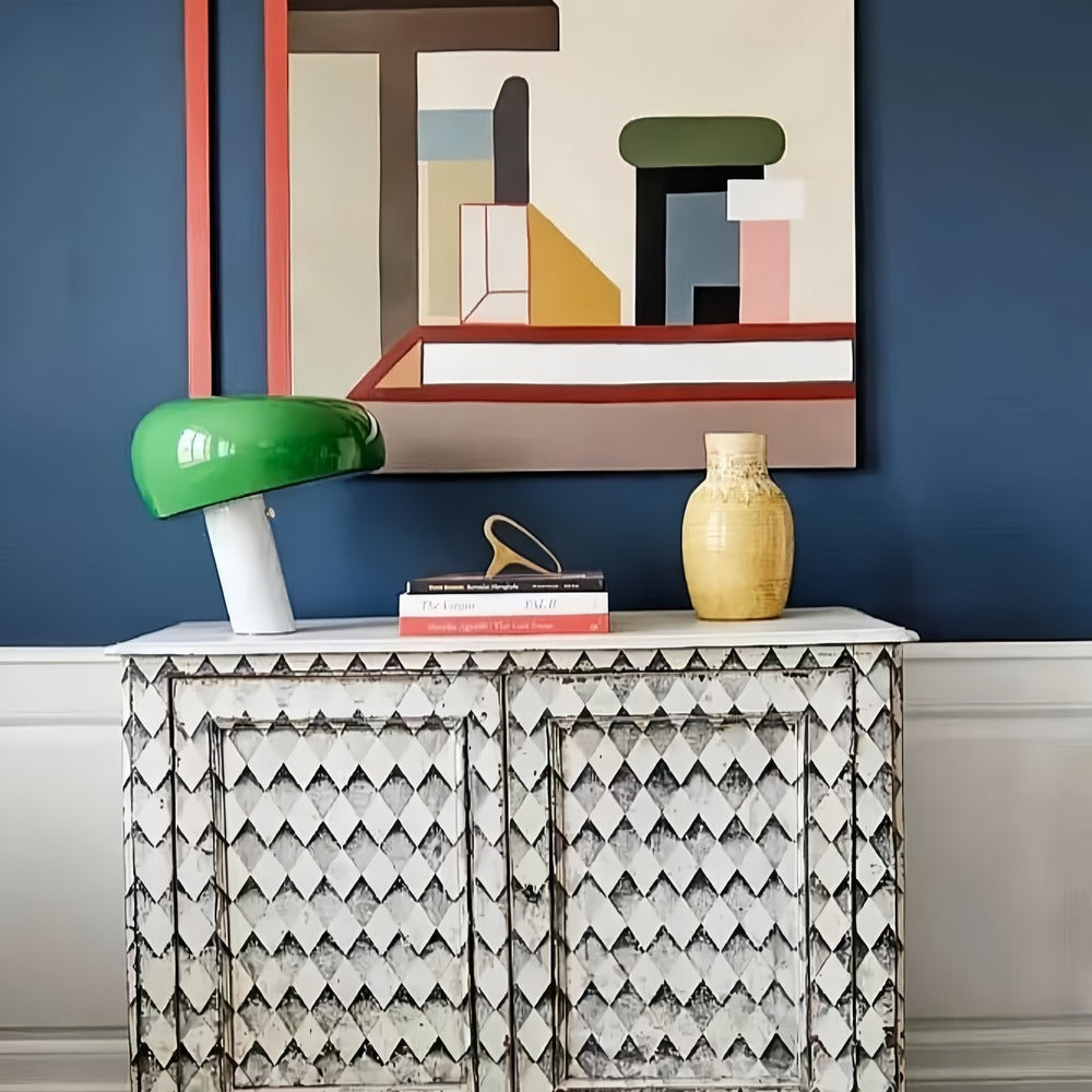Green marble table lamp on a patterned cabinet beneath framed artwork.