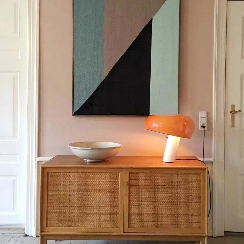 Orange marble table lamp on a woven-front cabinet beneath abstract art.