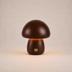 Dark brown mushroom table lamp with a short rounded base, gold button, and warm glow on a beige background.