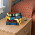 Stained glass book table lamp glowing on an oak nightstand beside a rust-colored quilt.
