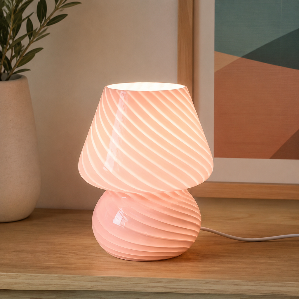 Pink swirled glass table lamp glowing on a wood console below wall art.