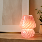 Pink swirled glass table lamp glowing beside framed abstract art.