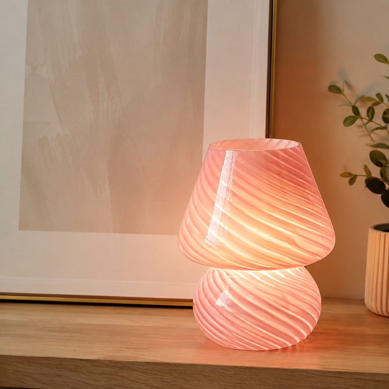 Pink swirled glass table lamp glowing beside framed abstract art.