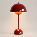 Glossy red table lamp with a dome shade, slim stem, rounded base, and warm light on a neutral background.