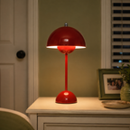 Red table lamp glowing on a white bedside cabinet beside framed art and a small potted plant.