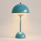 Teal table lamp with a rounded dome shade, slim stem, circular base, and warm downward glow.